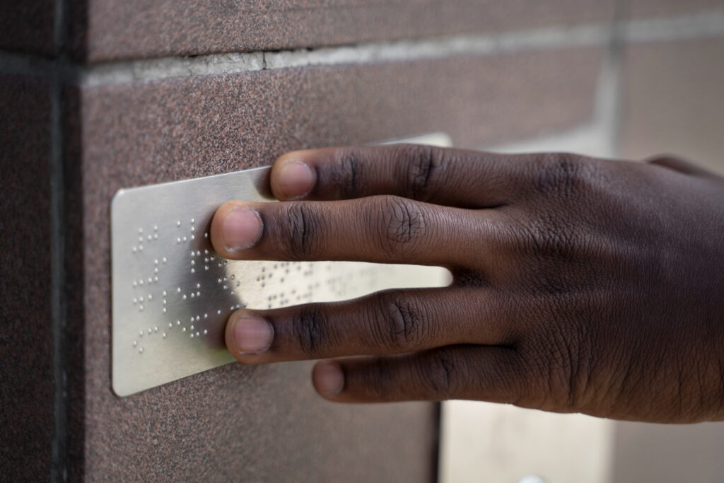 Person reading Braille signage on a wall for accessible navigation