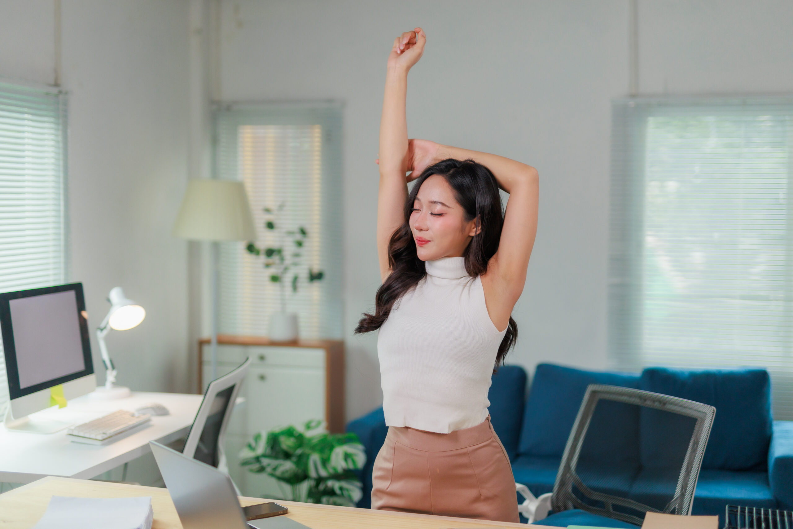 Woman stretching at her desk in a bright modern office environment.