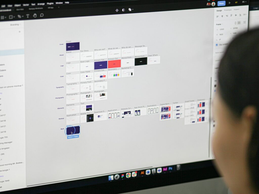 Designer using Figma on a desktop to organize UI components, website layouts, and brand assets for a collaborative digital design project.
